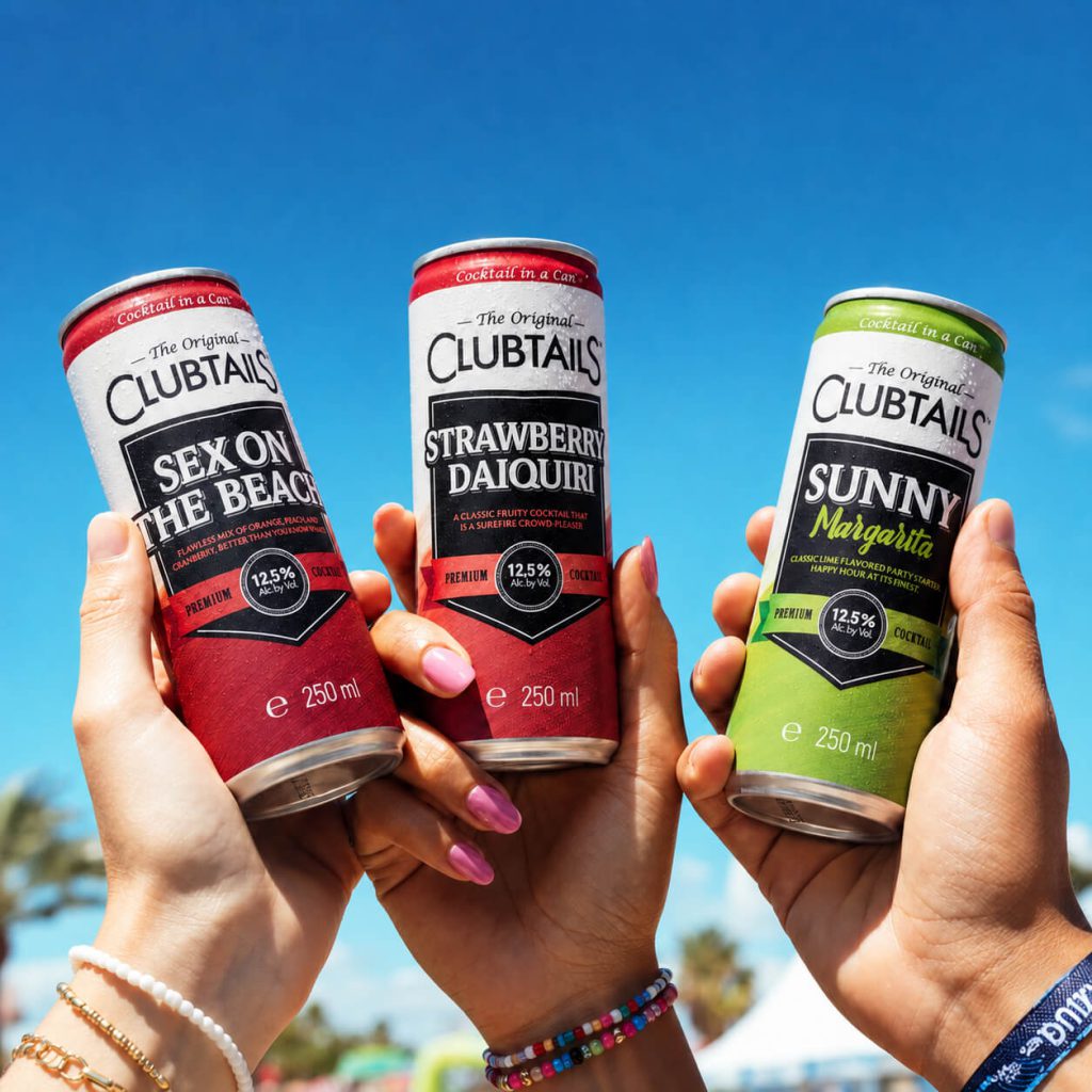 Friends raise Clubtails Sex on the Beach, Strawberry Daiquiri and Sunny Margarita cocktail cans under a blue sky.